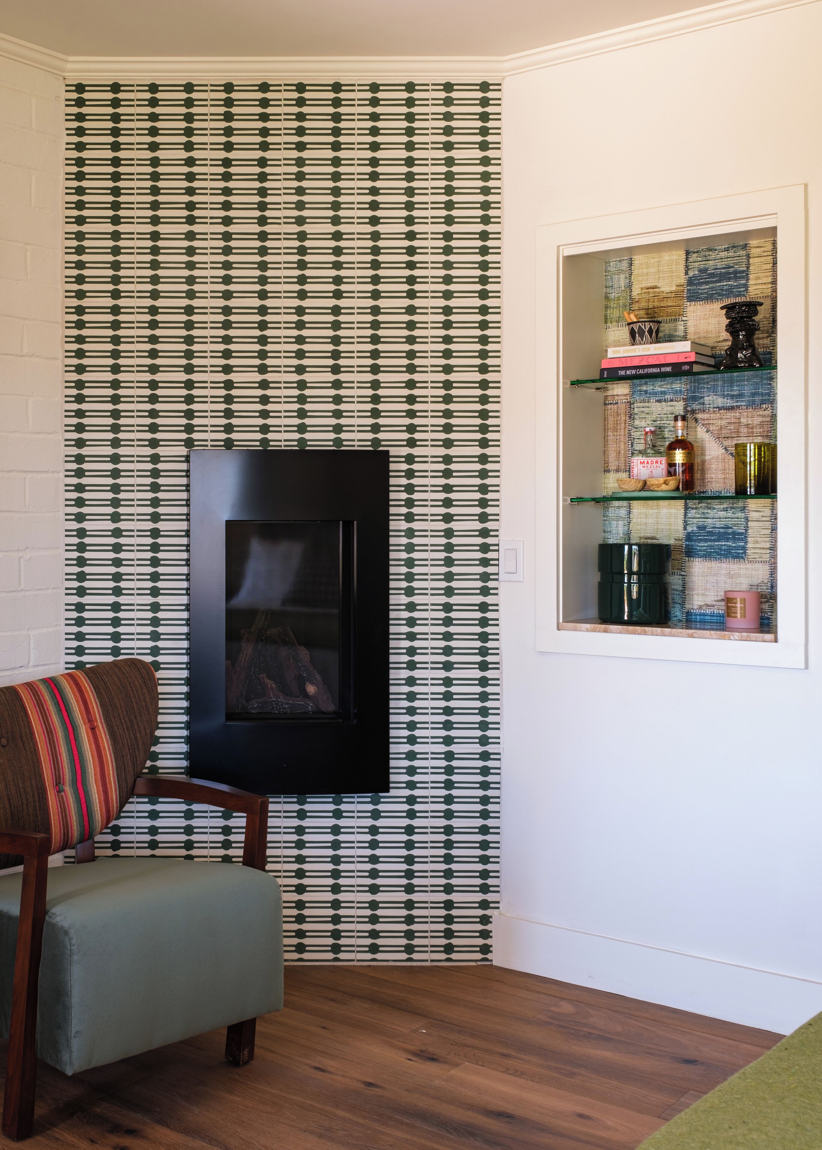 A living room with a fireplace, patterned wallpaper, a bookshelf, and a striped armchair.