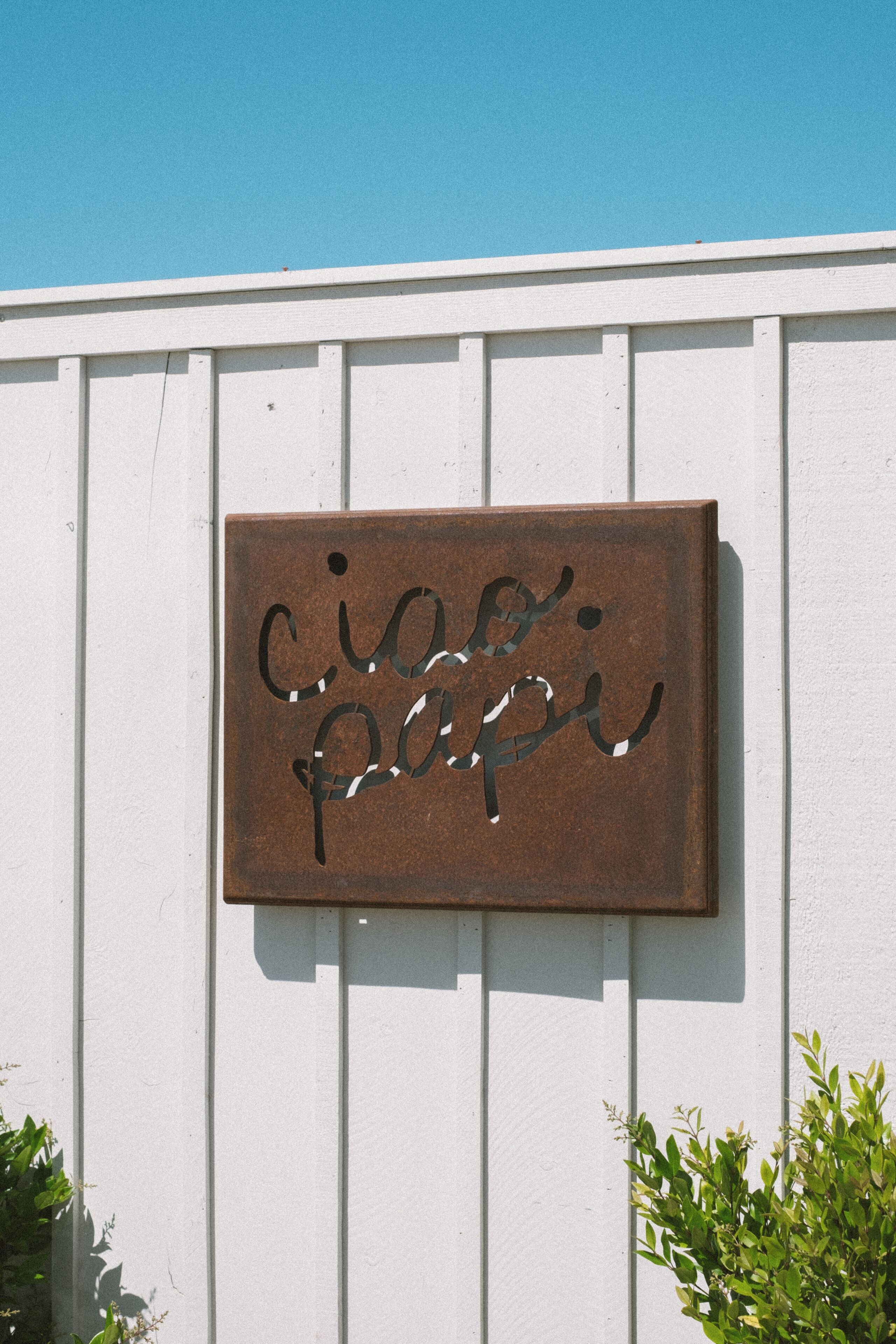 Une enseigne en métal au style rustique, portant les mots « cicco papi », fixée à un mur en bois peint en blanc.