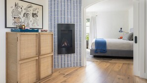 A modern bedroom with a fireplace, a bed with a blue blanket, a wooden wardrobe, and a patterned wall. - River Lodge Paso - 21 & Over Pool (Paso Robles)