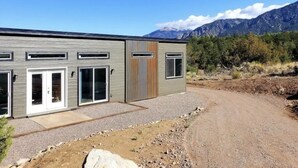 A modern building with a gravel driveway and a mountain backdrop. - Mountain Side Home with Spectacular Views!! 2bd-2ba - 420 & Dog Friendly + AC !! (Crestone)