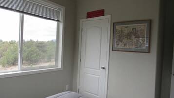 Une chambre à coucher avec un lit, une fenêtre avec des stores, une porte et un tableau encadré au mur.