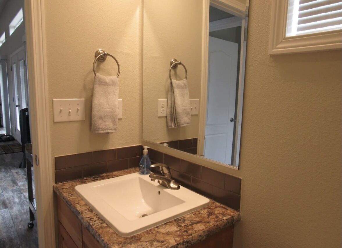 A bathroom with a white sink, granite countertop, and a mirror above it. There are two towels hanging on towel rings on the wall.