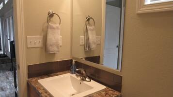 A bathroom with a white sink, granite countertop, and a mirror above it. There are two towels hanging on towel rings on the wall.