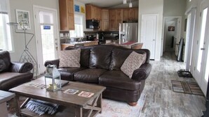 A spacious living room with a brown leather sofa, a wooden coffee table, and a kitchen in the background. - Mountain Side Home with Spectacular Views!! 2bd-2ba - 420 & Dog Friendly + AC !! (Crestone)