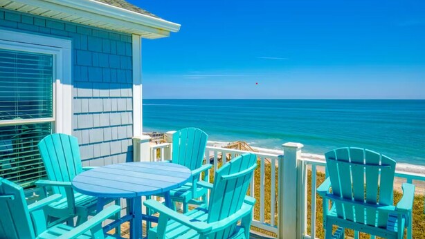 A coastal house with a balcony featuring turquoise Adirondack chairs and a table, overlooking the ocean. - Spacious Oceanfront | Sleeps 30!
 (North Topsail Beach)