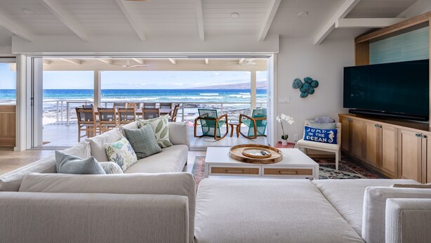 A spacious living area with a large window overlooking the ocean, a ceiling fan, a flat-screen TV, and a cozy seating arrangement.
