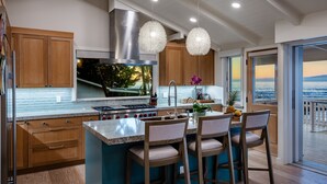 A modern kitchen with a large island, bar stools, a view of the ocean, and a built-in stove.
