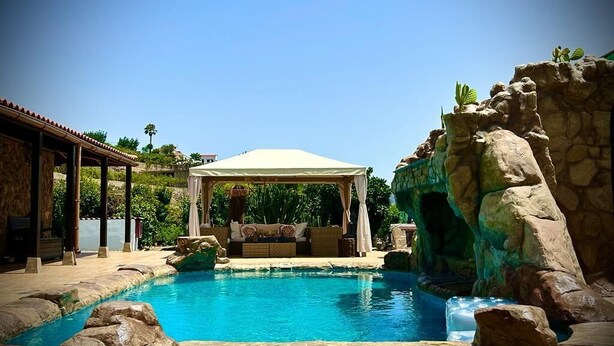 A pool area with a gazebo, rock formations, and a clear blue sky. -  Cabin with jacuzzi in its 800 meter private land with fruit trees.  (fataga)