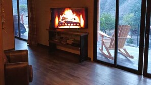 A living room with a fireplace, a television, and a sliding glass door leading to an outdoor area with chairs. -  Cabin with jacuzzi in its 800 meter private land with fruit trees.  (fataga)