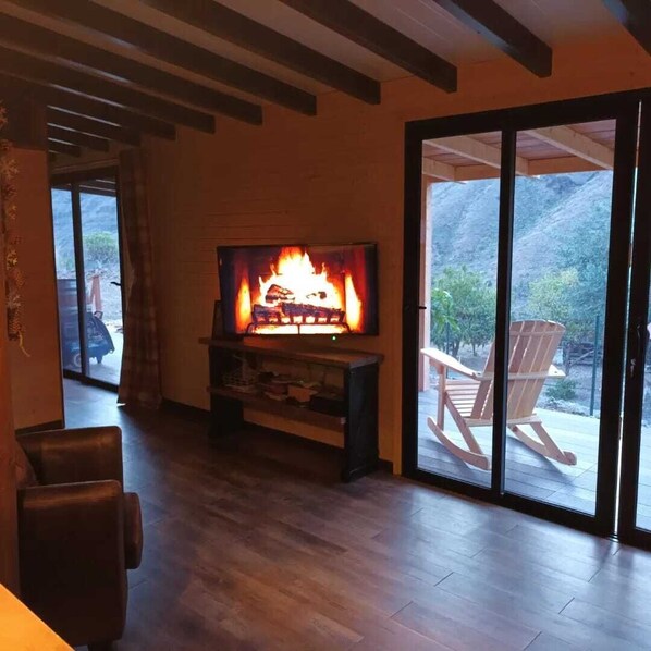 A living room with a fireplace, a television, and a sliding glass door leading to an outdoor area with chairs. -  Cabin with jacuzzi in its 800 meter private land with fruit trees.  (fataga)