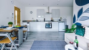 A modern kitchen with white cabinets, a built-in oven, and a dining area with a wooden table and benches.