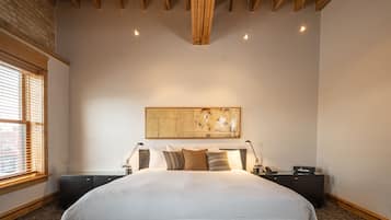 Un dormitorio con una cama grande, vigas de madera en el techo, un cuadro abstracto de gran tamaño y una ventana con persianas.