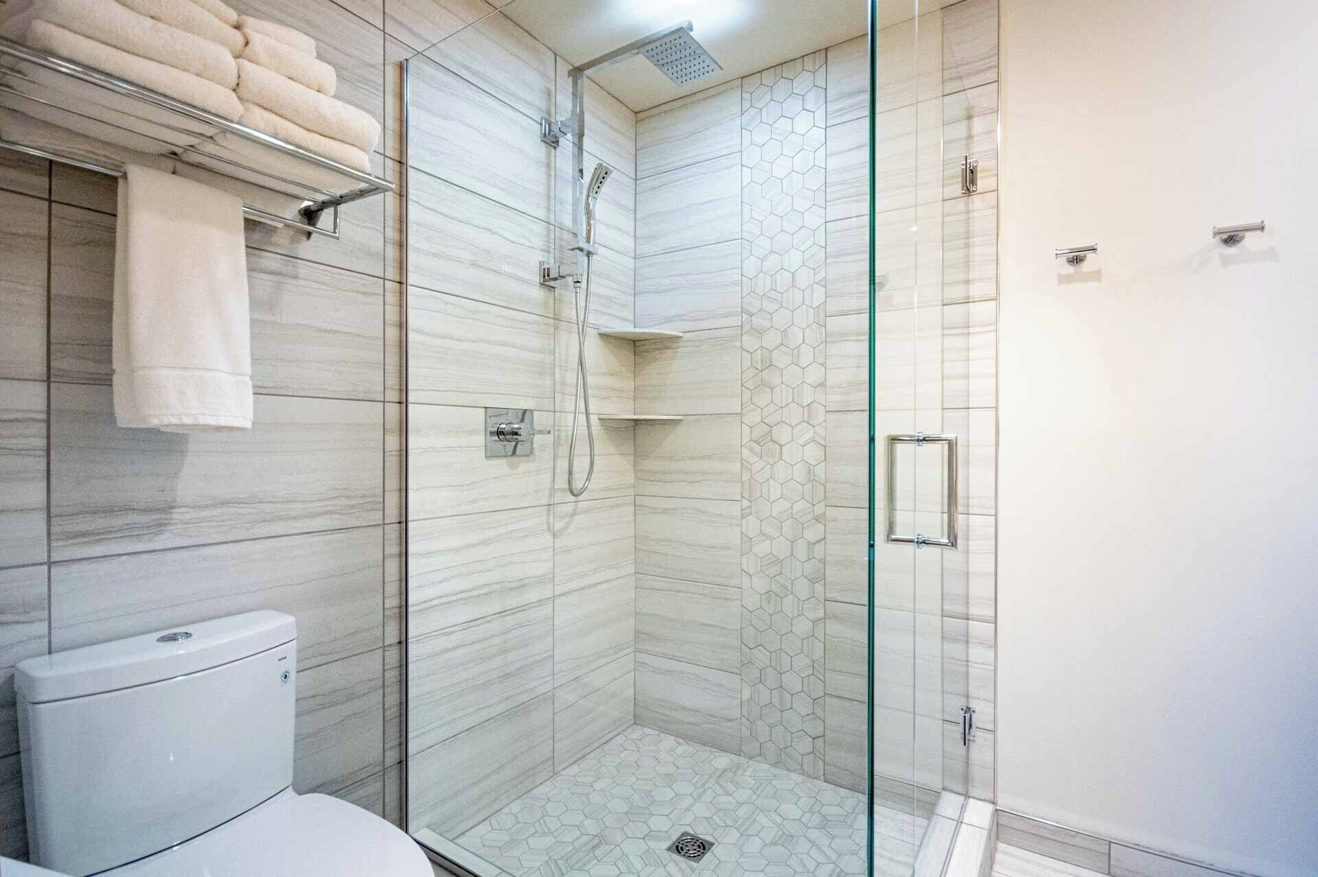 A modern bathroom with a glass-enclosed shower, a toilet, and a towel rack.