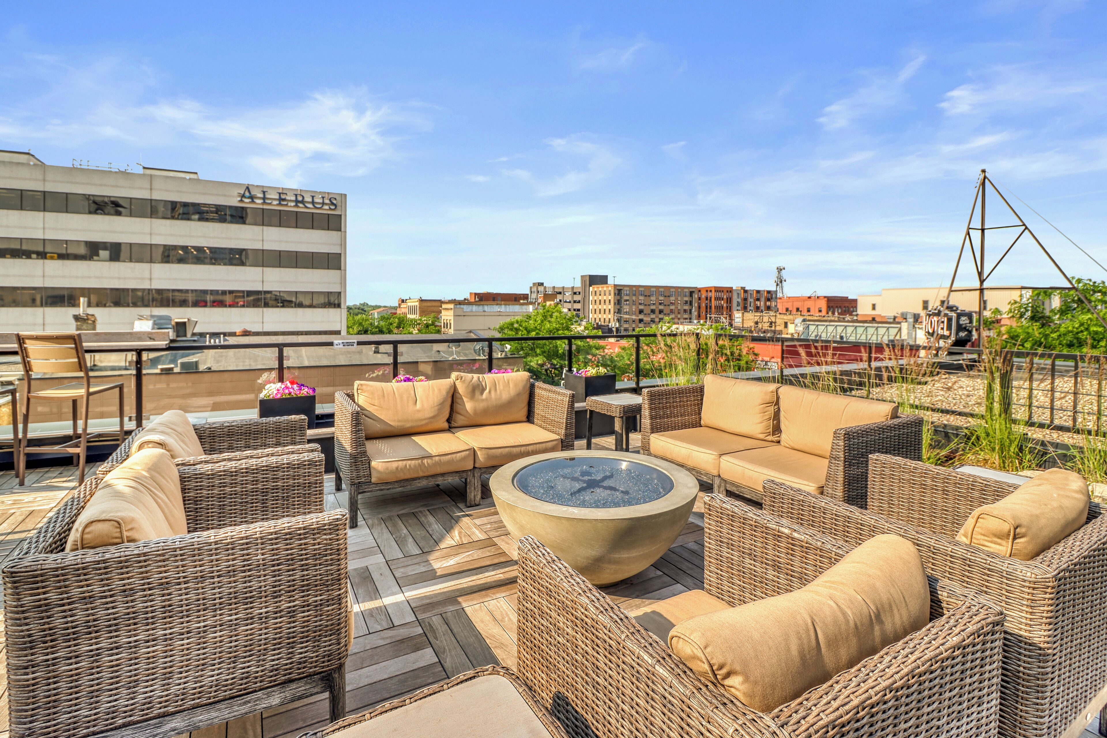 A rooftop terrace with wicker furniture, a fire pit, and a view of the cityscape.