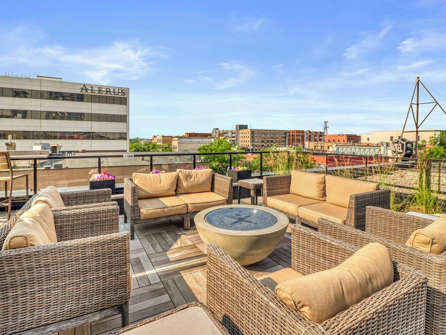 Um terraço no telhado com mobiliário de vime, uma lareira e vista para a paisagem urbana.