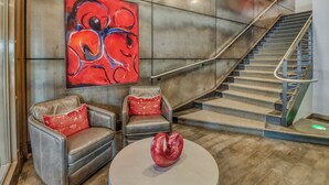 A modern lobby with a staircase, leather armchairs, a red abstract painting, and a unique red sculpture. - Hotel Donaldson (Fargo)
