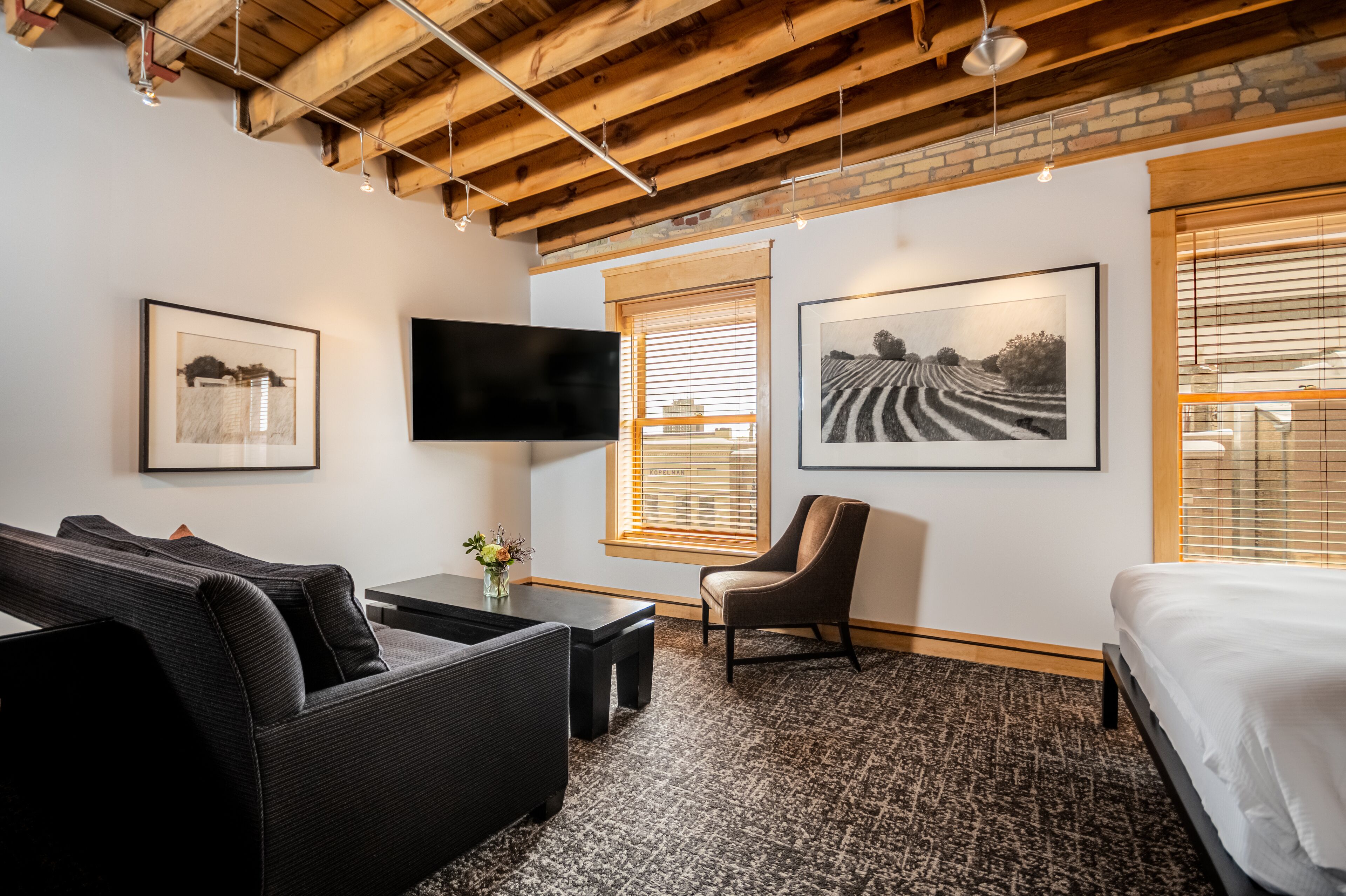 Une chambre d’hôtel moderne avec un canapé noir, une petite table surmontée d’un vase, un fauteuil en cuir, un lit et des œuvres d’art accrochées aux murs.