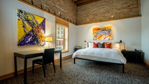 A bedroom with a bed, desk, chair, and two paintings on the walls. - Hotel Donaldson (Fargo)