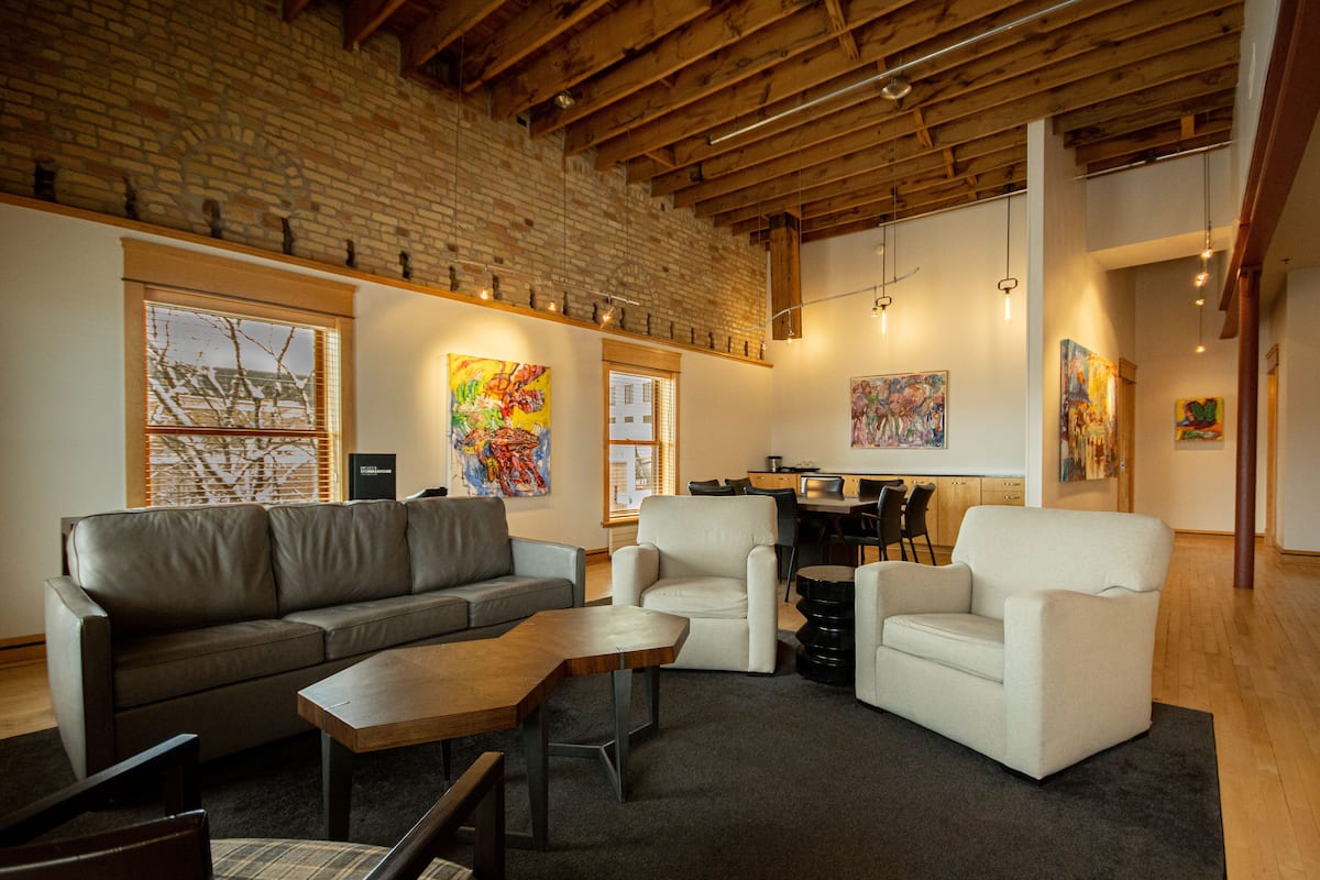 Un salon moderne avec un mur en briques, des poutres en bois au plafond et des œuvres d’art accrochées aux murs.