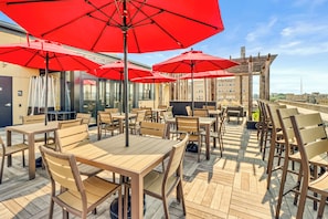 An outdoor seating area with wooden tables and chairs, red umbrellas, and a view of the cityscape. - Hotel Donaldson (Fargo)
