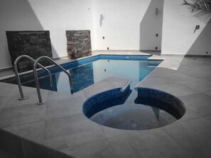 A swimming pool with a stone wall and a small circular hot tub. - Refugio Acolchado: Habitaciones Dobles para Humanos y Peludos Compañeros (Ciudad Madero)