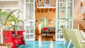 An open-plan living area with a wooden floor, a red bench, a green sofa, and a staircase leading to an upper level. - Flower of Life (Limon Province)