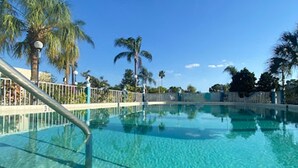 A clear blue pool with a metal railing, surrounded by palm trees and a clear sky. - Bposhtels Clearwater Tampa (Clearwater)