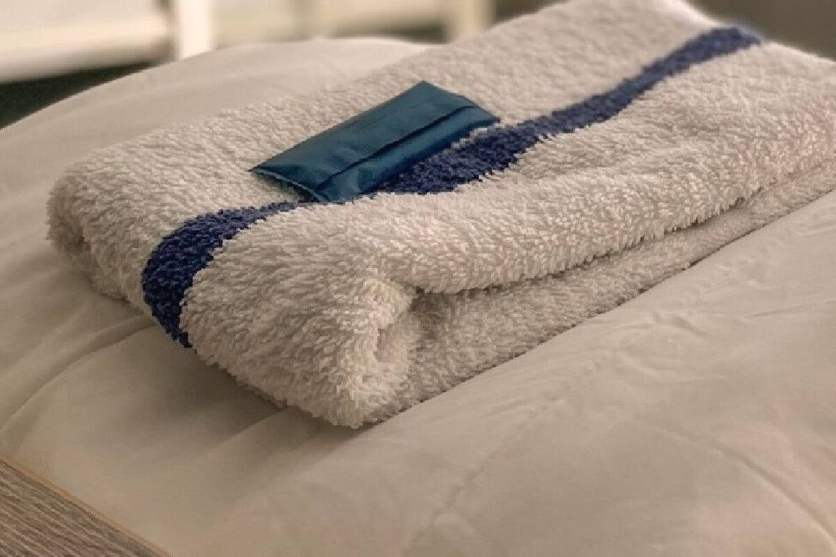 A neatly made bed with a white pillow and a folded towel with a blue stripe.