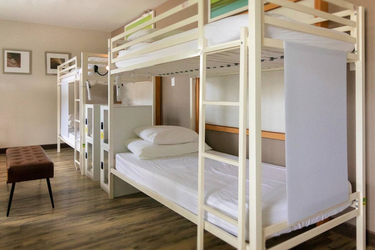 A bunk bed room with a wooden floor, a bench, and a wall-mounted shelf.