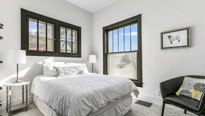 A bedroom with a large bed, two windows, a chair, and a lamp. - Restored farmhouse in Old Town Loveland

 (Loveland)