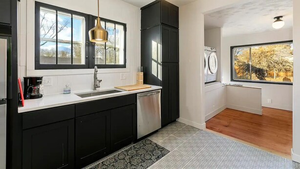 A modern kitchen with black cabinets, a stainless steel dishwasher, a coffee maker, and a large window with a view of trees. - Restored farmhouse in Old Town Loveland

 (Loveland)