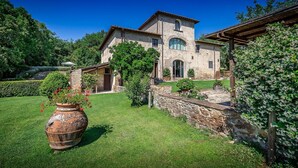 A rustic stone building with a garden in front, a large pot with flowers, and a clear blue sky.