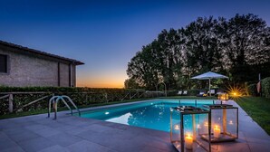 A swimming pool with a glass enclosure and candles, surrounded by a paved patio and a hedge.