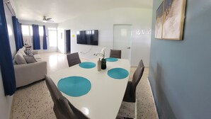 Un saló modern amb un sofà blanc, una taula de dinar amb suportes blaus i un televisió de pantalla plana penjada a la paret.