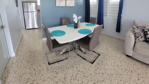 Un espai vital compacte amb una cuineta, una zona de menjador amb una taula blanca i salveta blava, i un sofà amb coixinets estampats.
