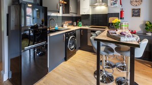 A compact kitchen with a refrigerator, washing machine, and a small dining area with stools.