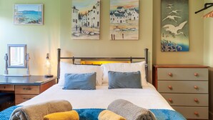 A neatly made bed with two pillows, a blue blanket, and two rolled towels.