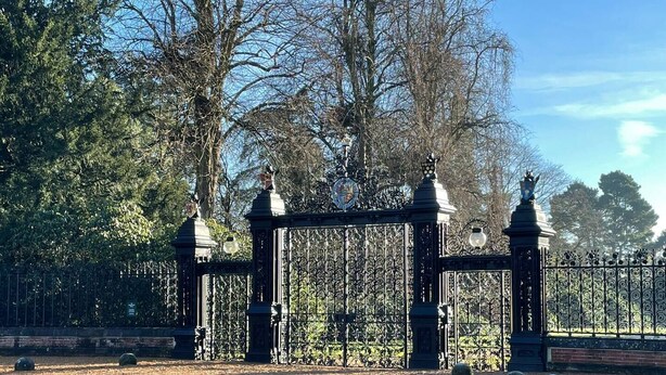 A gated entrance with ornate ironwork, a clock, and a statue on top.
