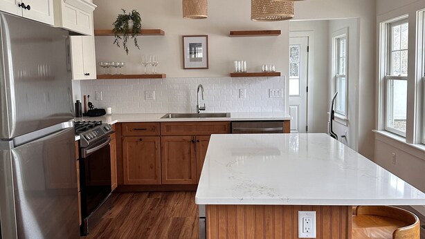 A modern kitchen with wooden cabinets, a stainless steel refrigerator, a large island, and pendant lighting. - Quick walk to private beach from this brand new 3-bedroom cottage (Wareham)