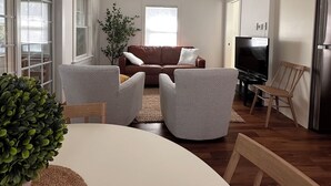 A spacious living area with a ceiling fan, a brown leather sofa, two armchairs, a dining table, and a kitchen area with a refrigerator. - Quick walk to private beach from this brand new 3-bedroom cottage (Wareham)