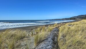 Ein Strand mit Wellen, grasbewachsenen Dünen und blauem Himmel.