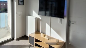 Una sala moderna con un televisor de pantalla plana montado en la pared, un mueble de entretenimiento de madera y una puerta a la derecha.