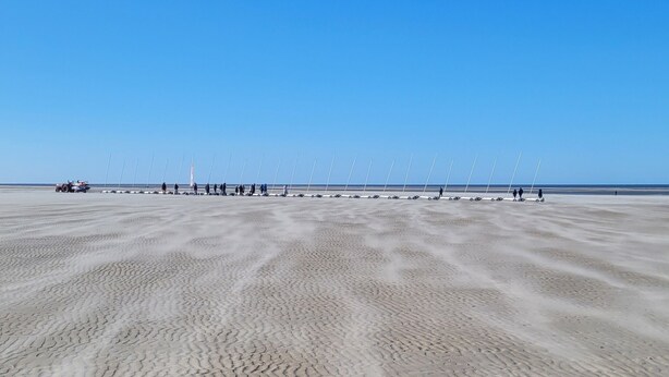 Una playa arenosa con huellas de neumáticos y un cielo azul despejado.