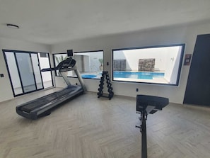 A spacious room with a treadmill, a stationary bike, and a large window overlooking a swimming pool. - Suite familiar 12 personas, cerca playa Miramar! (Ciudad Madero)