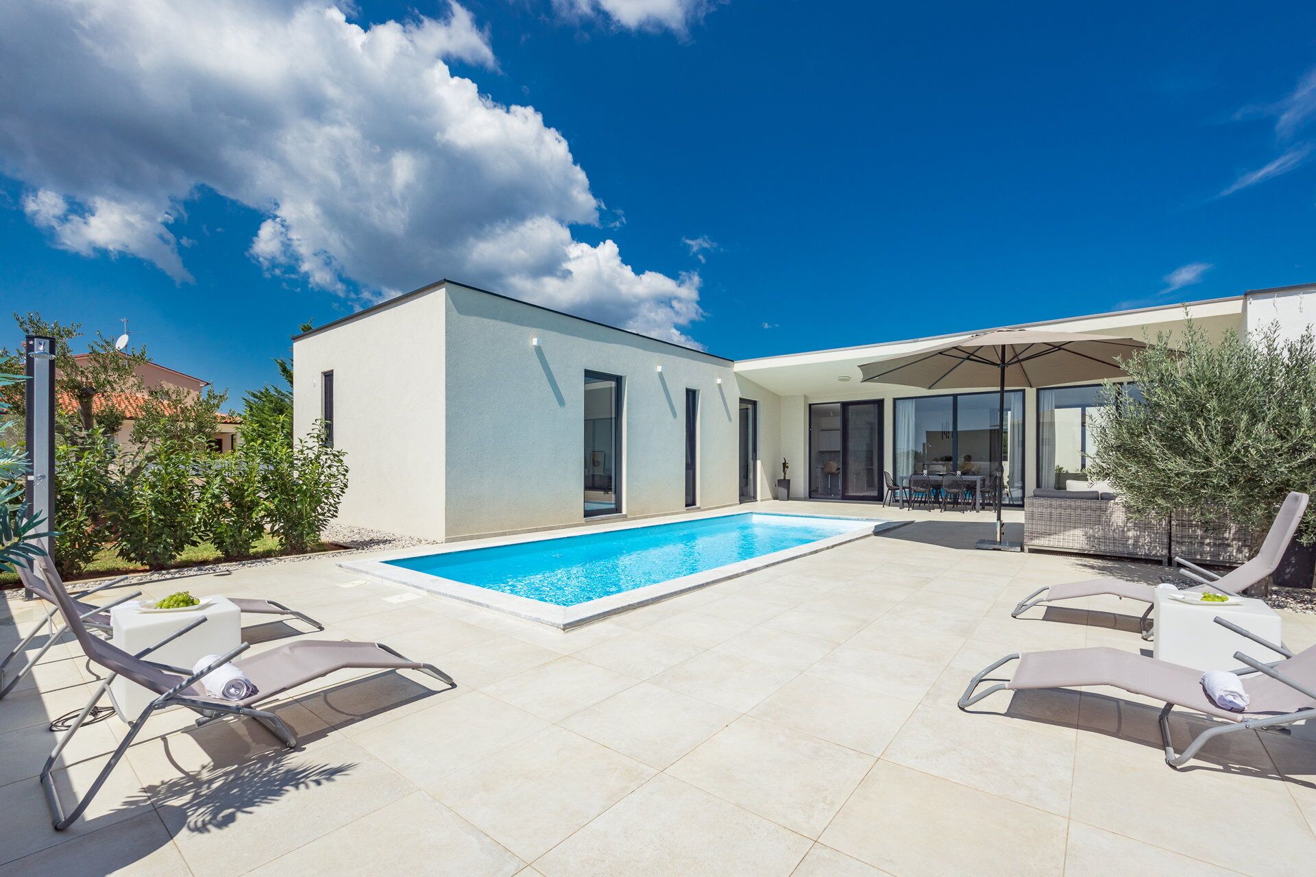A modern outdoor pool area with a rectangular pool, lounge chairs, and a covered seating area.