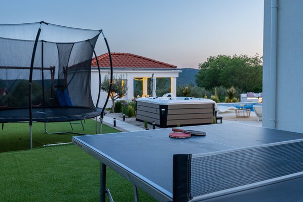 A ping pong table, a trampoline, and a hot tub in a backyard. - Villa Atticora with Pool (Radašinovci)