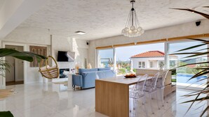 A spacious living area with a kitchen island, a blue sofa, and a dining area with transparent chairs. - Villa Atticora with Pool (Radašinovci)
