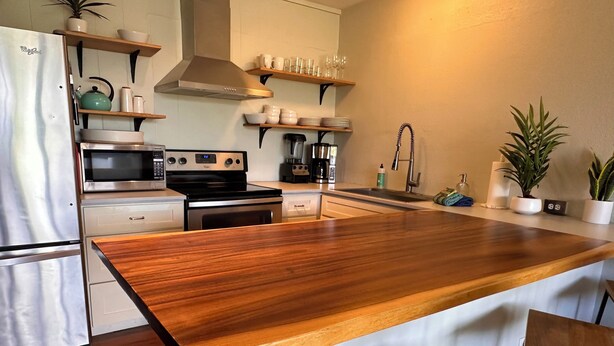 Een moderne keuken met een houten eiland, roestvrijstalen apparatuur en ingebouwde planken.