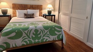 Een net opgemaakt bed met een groene en witte spreideken, twee bedlampen, een geweven hoofdbord, en een schilderij aan de muur.