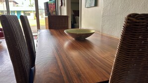 Een houten eettafel met een groene kom in het midden, omringd door rieten stoelen.